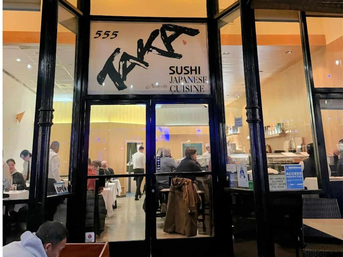Street view of Taka, a Japanese restaurant in San Diego's Gaslamp Quarter, with large front windows showing diners inside enjoying sushi beneath soft lighting. The restaurant sign reads “555 Taka Sushi Japanese Cuisine.”