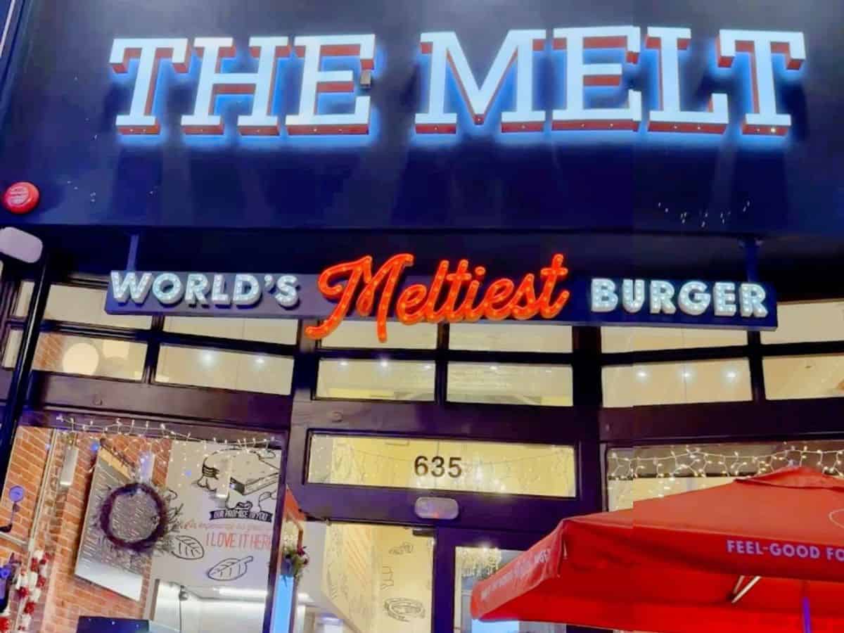 Exterior of The Melt restaurant at night, with bright marquee-style signage reading “WORLD’S Meltiest BURGER” above the entrance, which is decorated with fairy lights and a red umbrella outside.