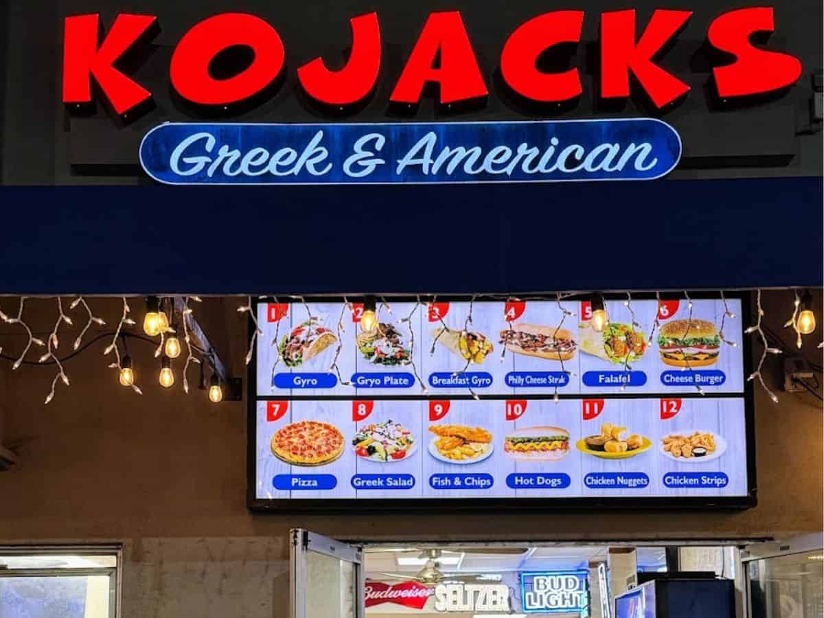 Entrance of Kojack's Greek & American Diner with a brightly lit menu board displaying various dishes. Patrons can be seen dining inside, emphasizing its reputation as one of the best restaurants in Mission Beach, San Diego.