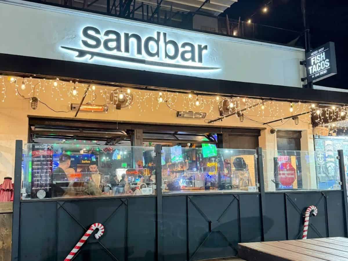 Nighttime view of Sandbar with its lit signage and festive decorations. The image shows the outdoor seating area and a glimpse of the bustling interior, capturing the energetic ambiance of one of the best bars in Mission Beach, San Diego.
