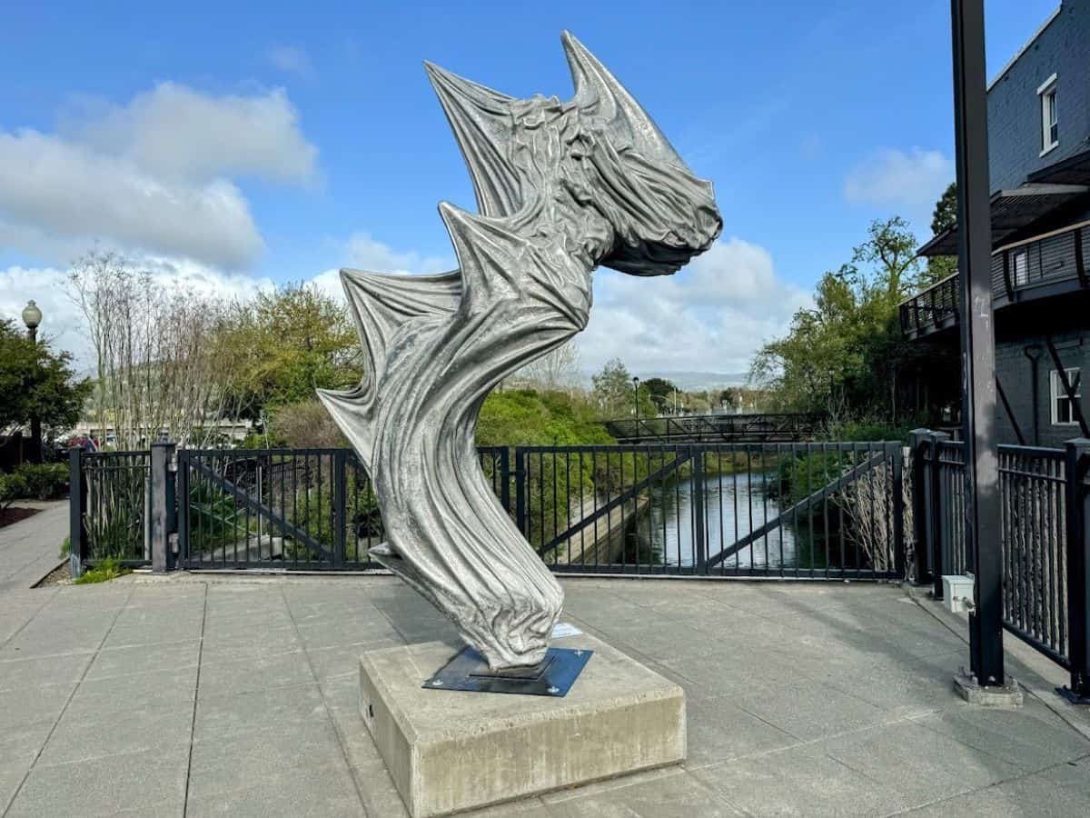 Abstract silver sculpture on the Downtown Napa Art Walk, set against a creek and vibrant trees—one of the many artistic stops to include in the 17 things to do in Napa.
