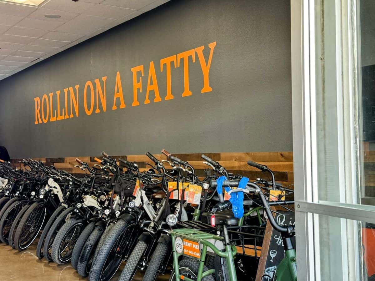 A row of electric fat tire bikes lined up inside a shop with a bold orange wall sign reading "ROLLIN ON A FATTY"—a fun and eco-friendly option among the 17 things to do in Napa.