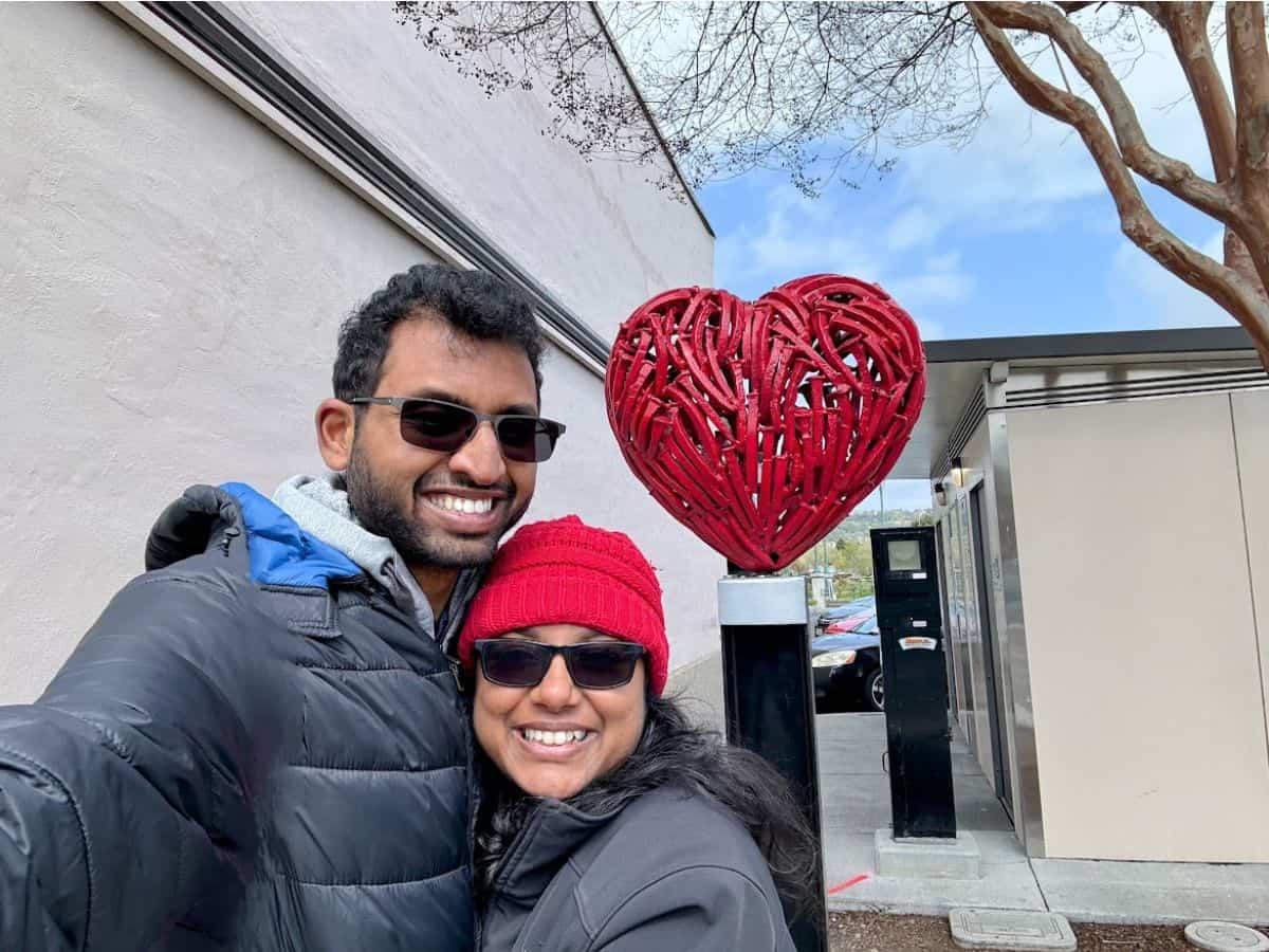Smiling couple taking a selfie in front of a red heart-shaped sculpture made of intertwined branches in downtown Napa—capturing the charm, love, and unforgettable moments that make up the 17 things to do in Napa.