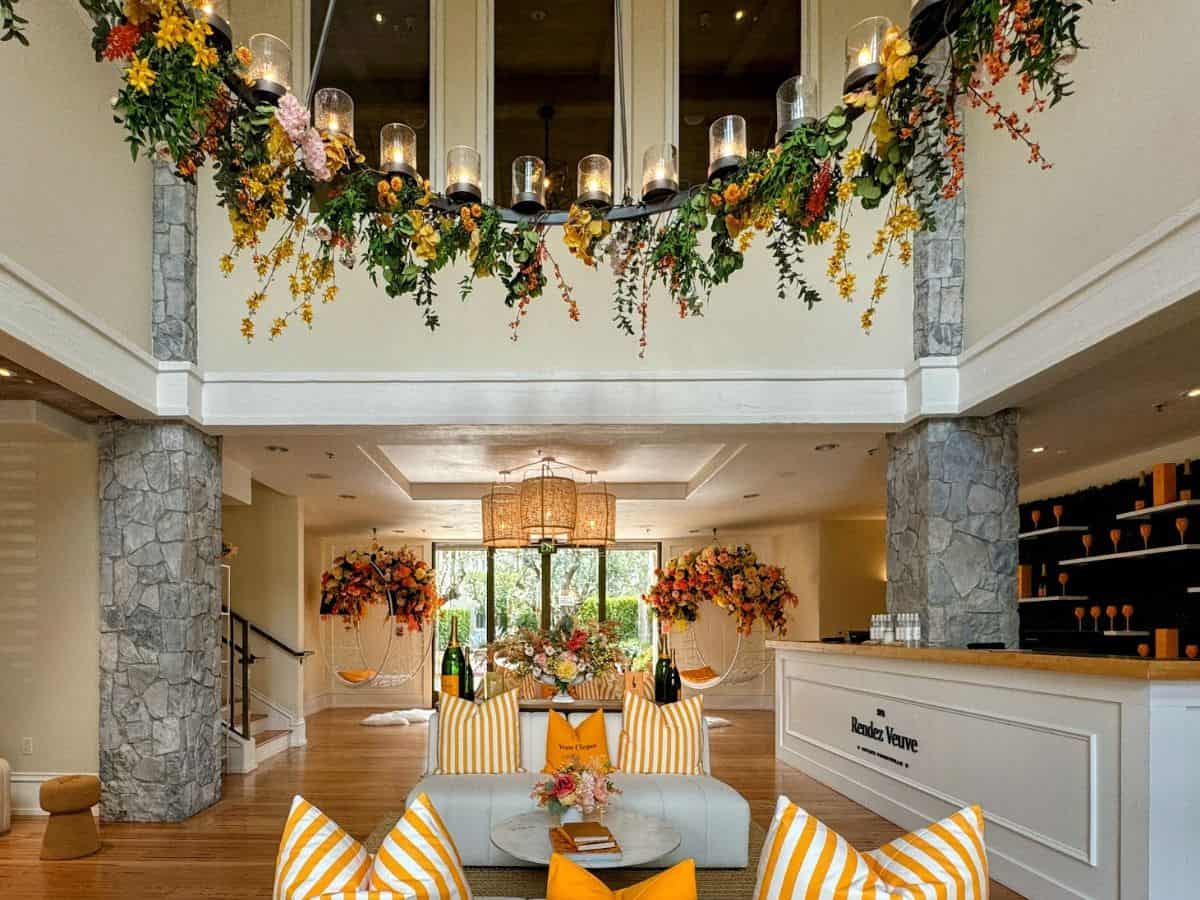 A bright and luxurious spa lobby with yellow-and-white striped pillows, hanging chairs adorned with flowers, and a garland of greenery and candles draped above. Relaxing at The Spa at Estate Yountville is one of the most rejuvenating things to do in Yountville.