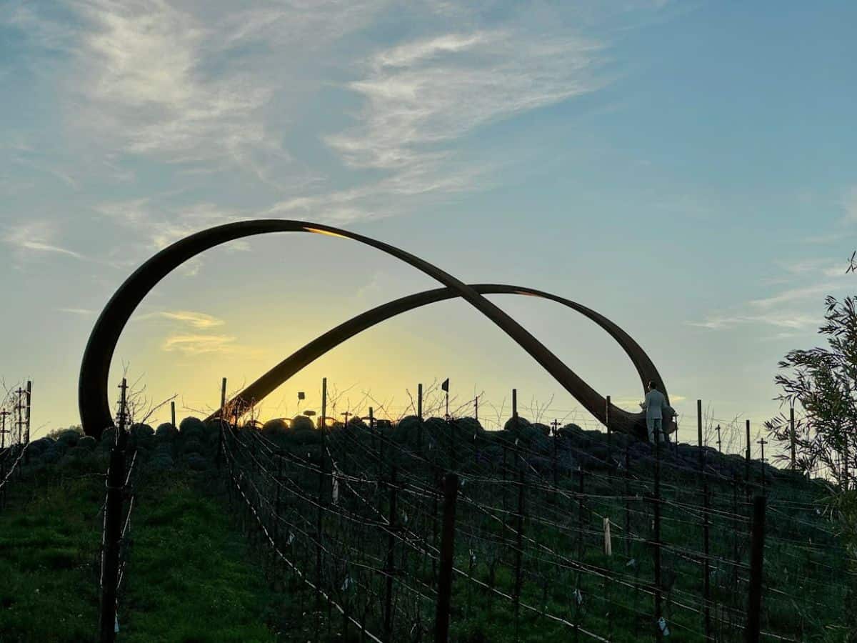 Sunset view of Infinity Hill with vineyard rows and a giant metal infinity sculpture overlooking the valley—perfect for soaking in the scenery on your journey through the 17 things to do in Napa.