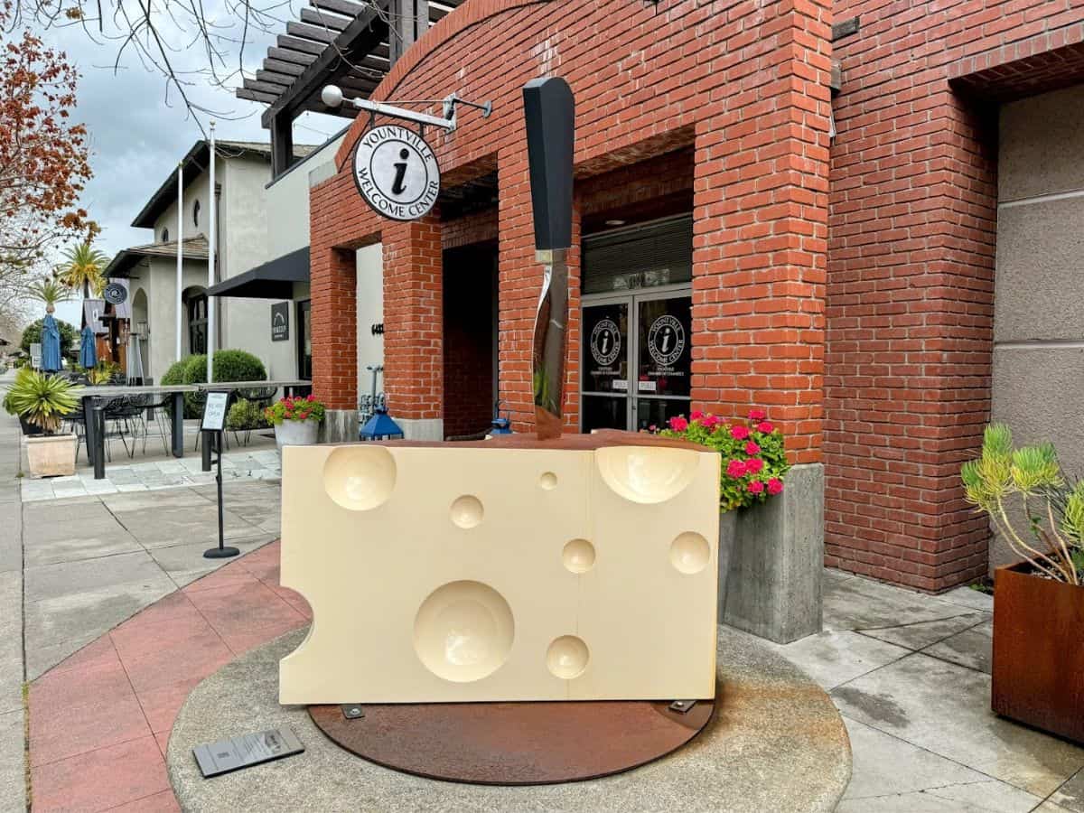 A whimsical oversized cheese sculpture with a giant fork stands in front of the red-brick Yountville Welcome Center. Starting your trip here is a smart and informative first step when exploring things to do in Yountville.