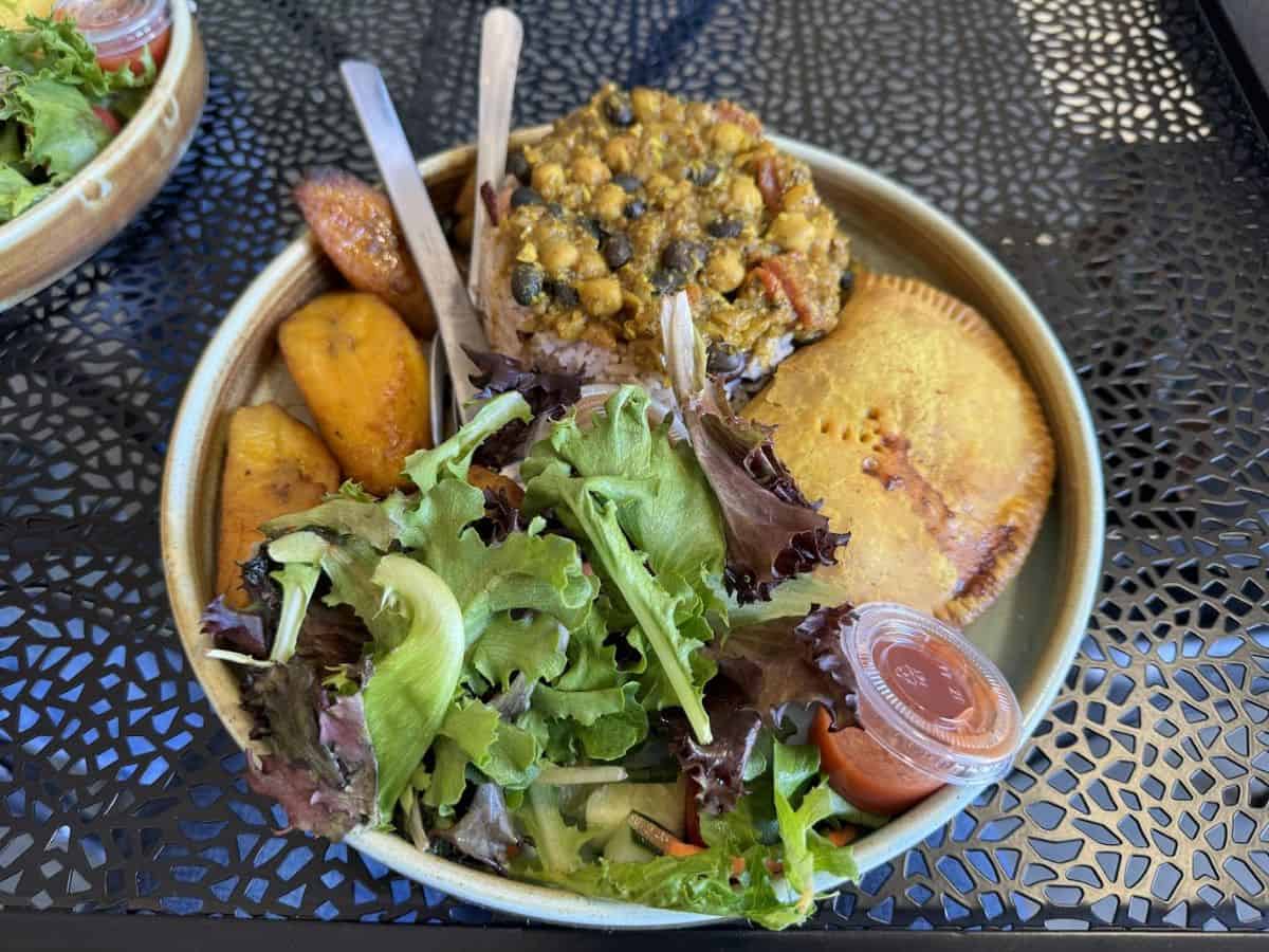 A plate with curried chickpea rice, fried plantains, salad, and a patty from Peaches & Patties at the Ferry Building, featured as one of the Best Spots to eat in San Francisco.
