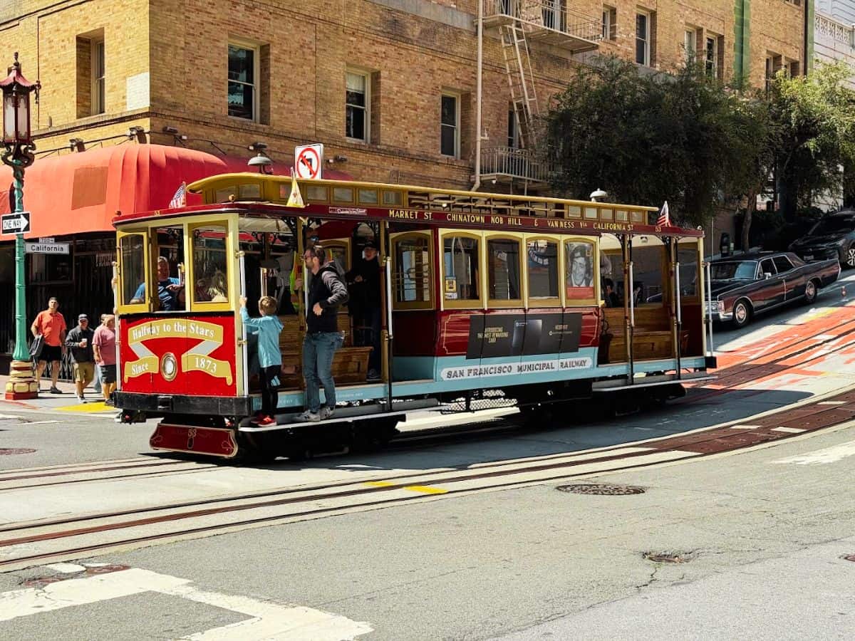San Francisco cable car carrying passengers uphill near Fisherman’s Wharf on a sunny day