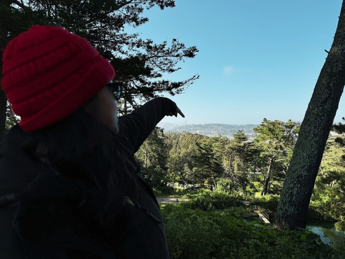 Vibrant woman pointing at San Francisco skyline from forested area, outdoor exploration in Bay Area.