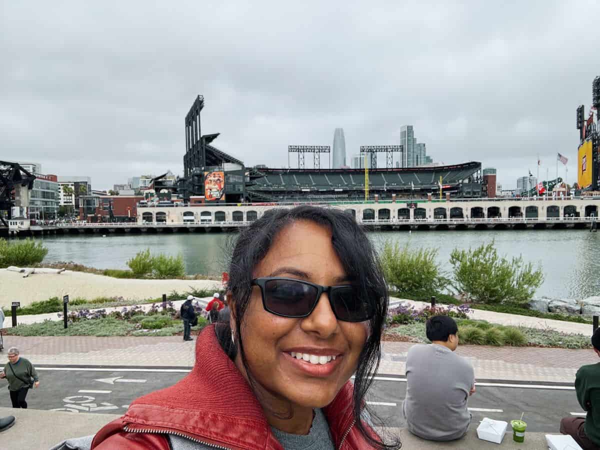 Vibrant woman smiling near San Francisco bay with the city skyline and Oracle Park stadium in the background.