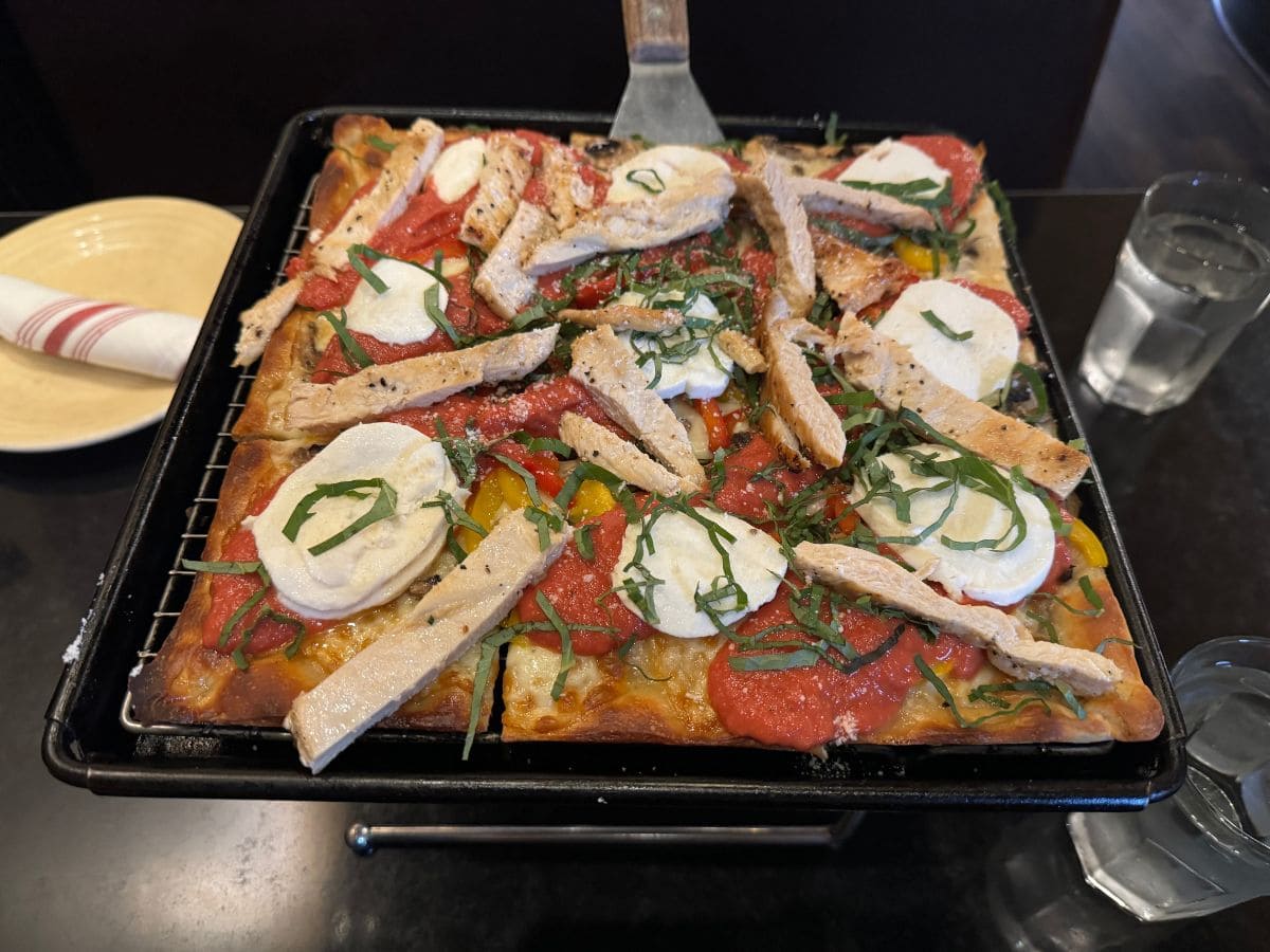 A tray of Detroit-style pizza with mozzarella, chicken, basil, and tomato sauce at Tony’s Pizza Napoletana, one of the Best Spots to eat in San Francisco.